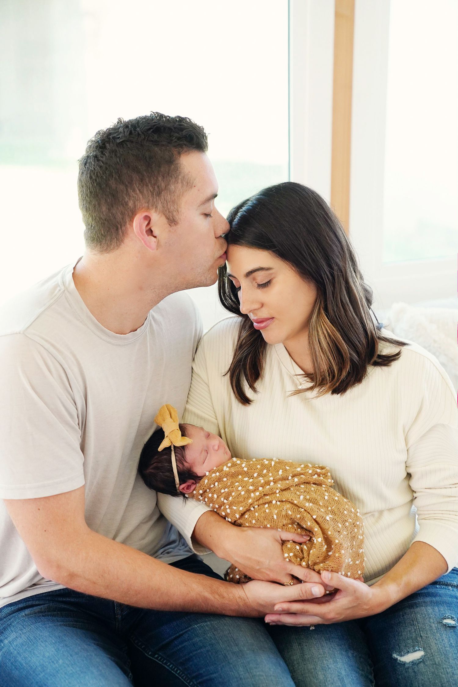 Intimate moment between couple holding sleeping newborn wrapped in sparkly gold swaddle.
