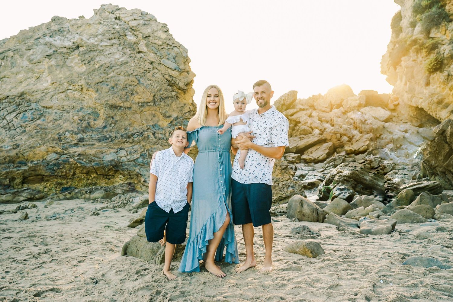 Family portrait on rocky beach with golden sunset backdrop.