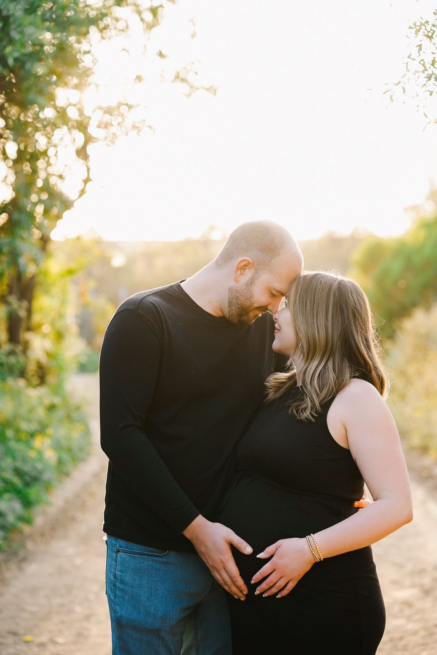 Tender embrace during sunset on a nature path with golden light filtering through trees.