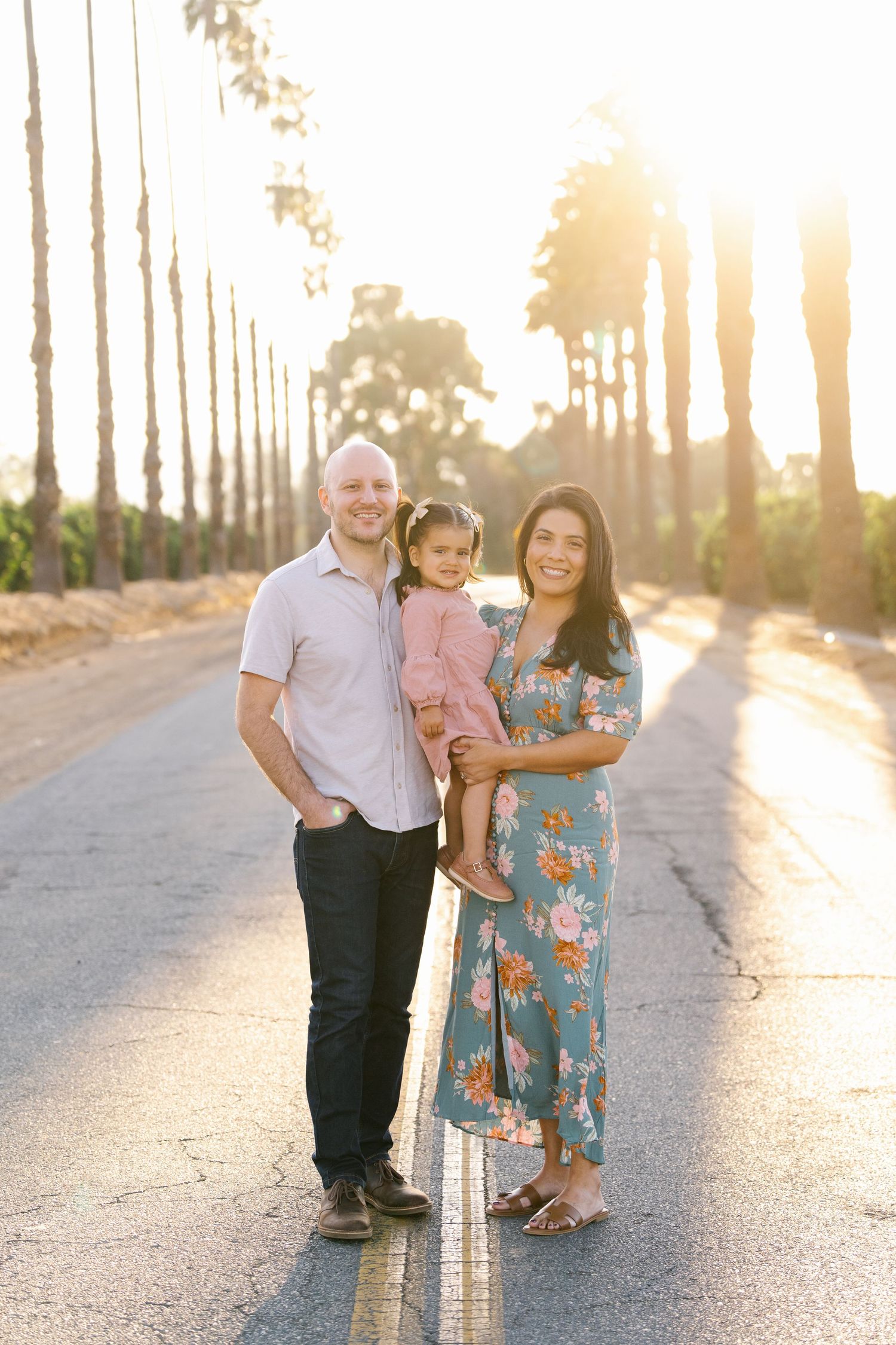 Family portrait on tree-lined road during golden hour sunset.