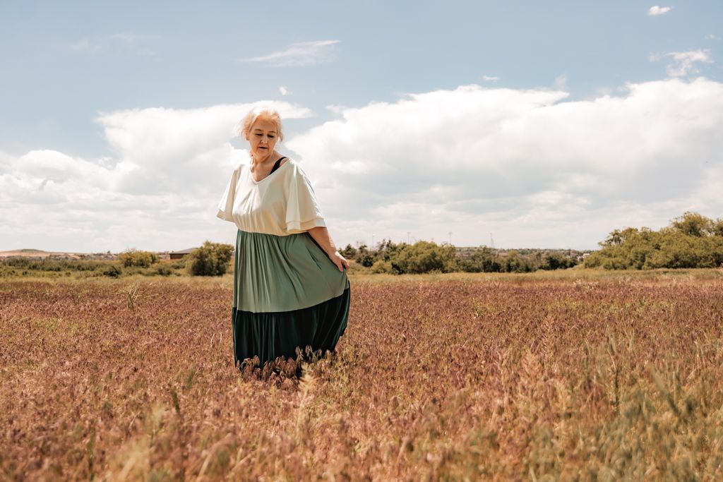 Woman wearing a flowing tiered dress standing in a vast golden field under blue skies.