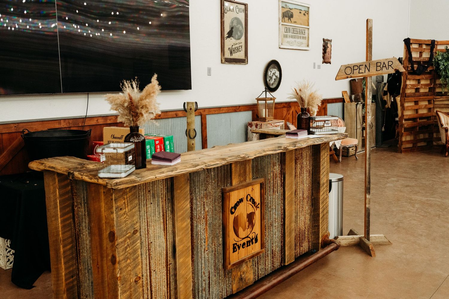Rustic wooden open bar setup with pampas grass decor and string lights at an event venue.