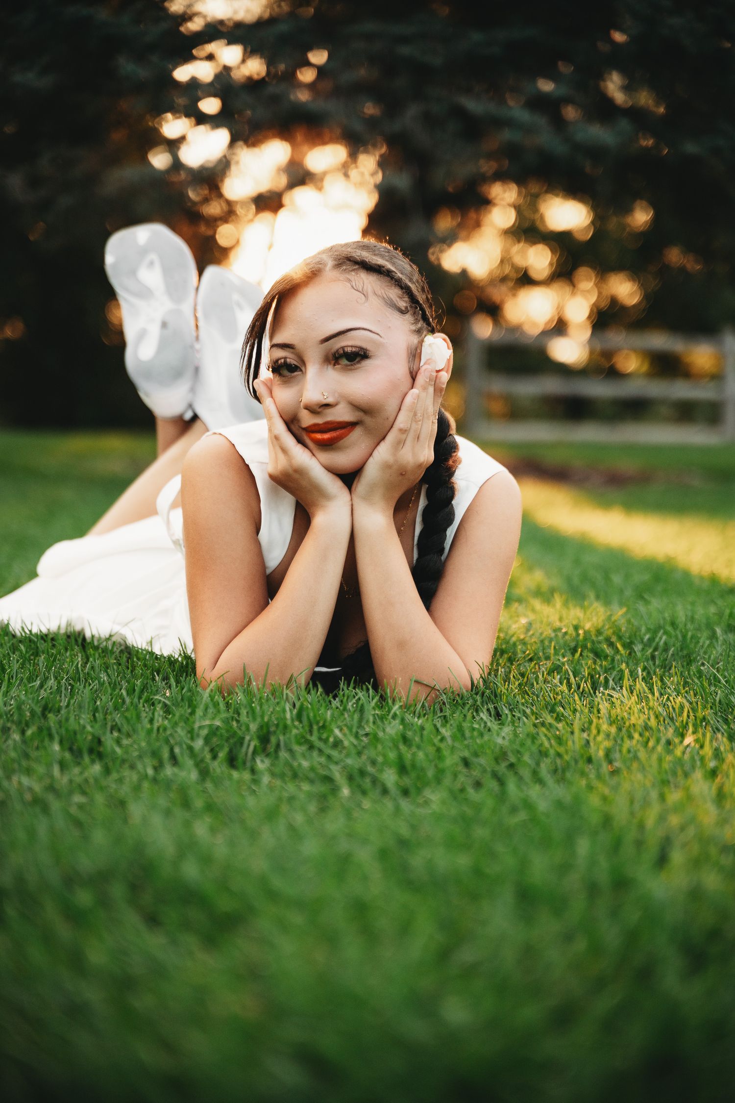 Someone in a white dress lying on green grass during golden hour sunset.