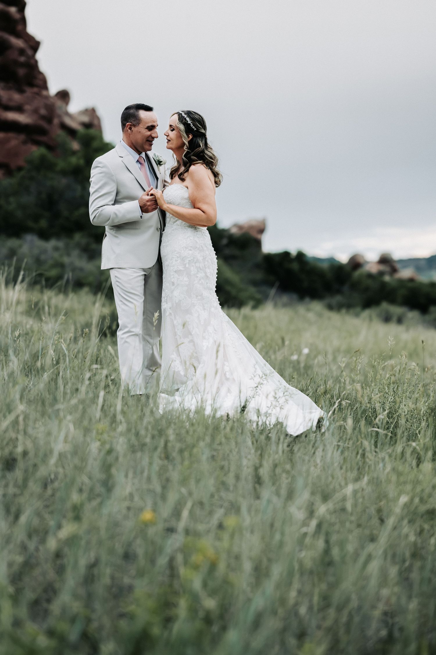A bride and groom share a romantic moment in a lush green meadow with red rock formations in the background.