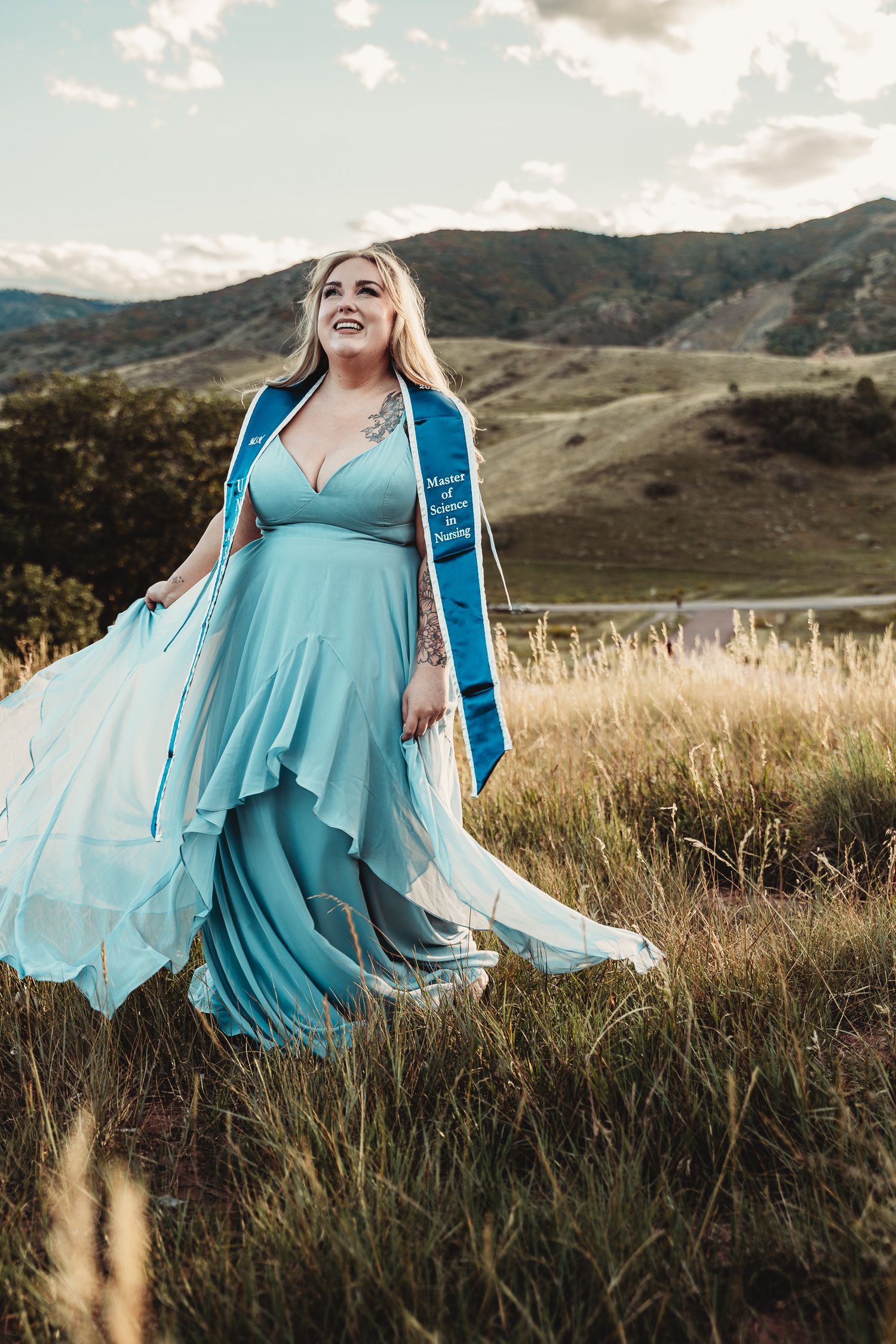 A flowing turquoise dress billows in the wind against a scenic mountain landscape at sunset.