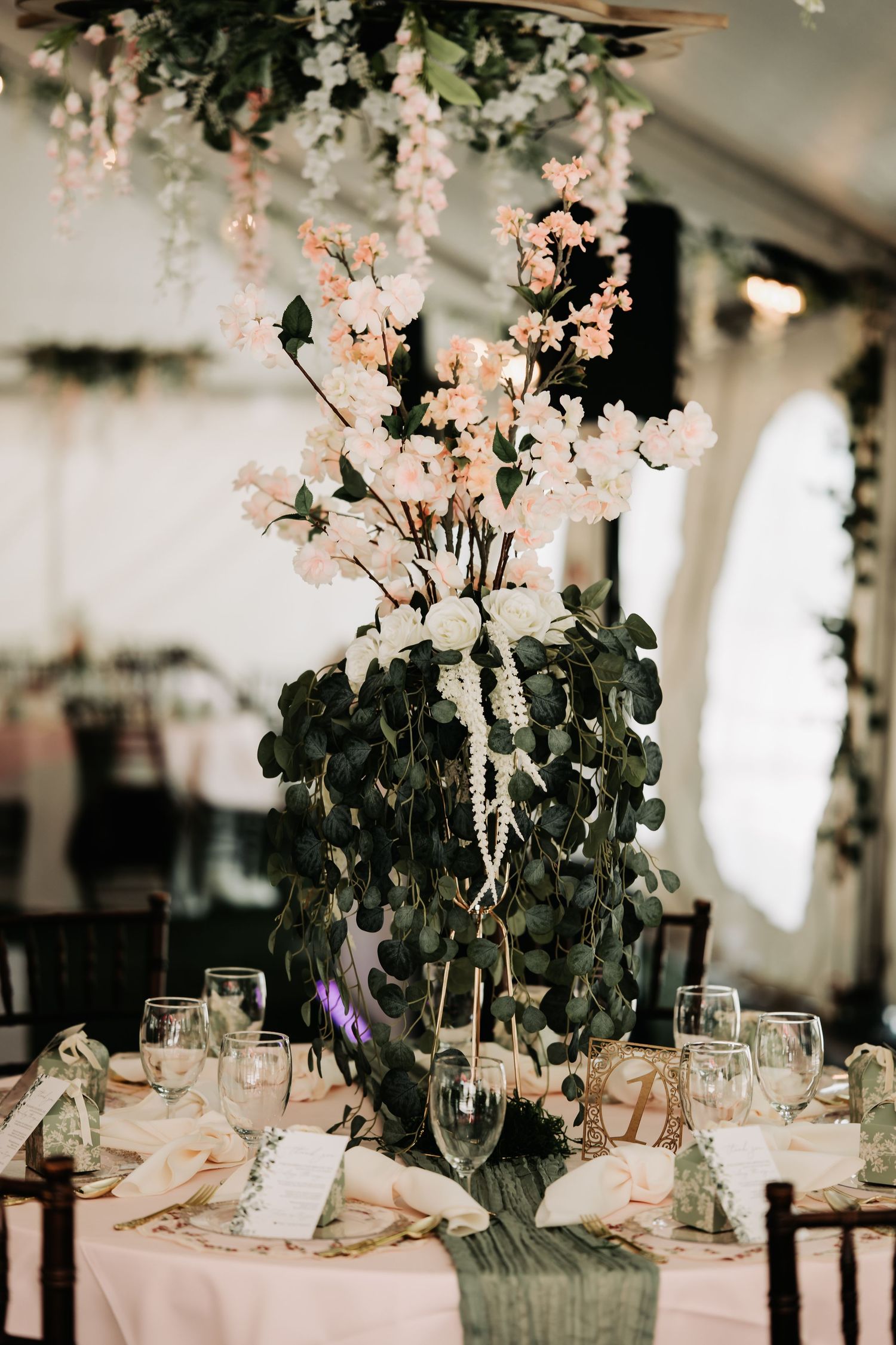 Elegant wedding reception table with tall floral centerpiece featuring white cherry blossoms, eucalyptus, and pearl strands.