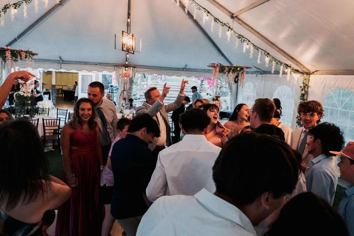 Guests dancing and celebrating under a white tent with string lights at a lively wedding reception party.