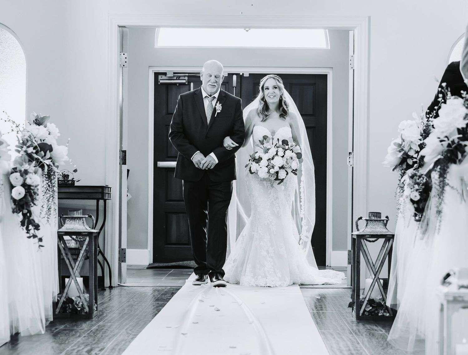 Black and white photo of a bride walking down the aisle with her father at an elegant wedding ceremony.