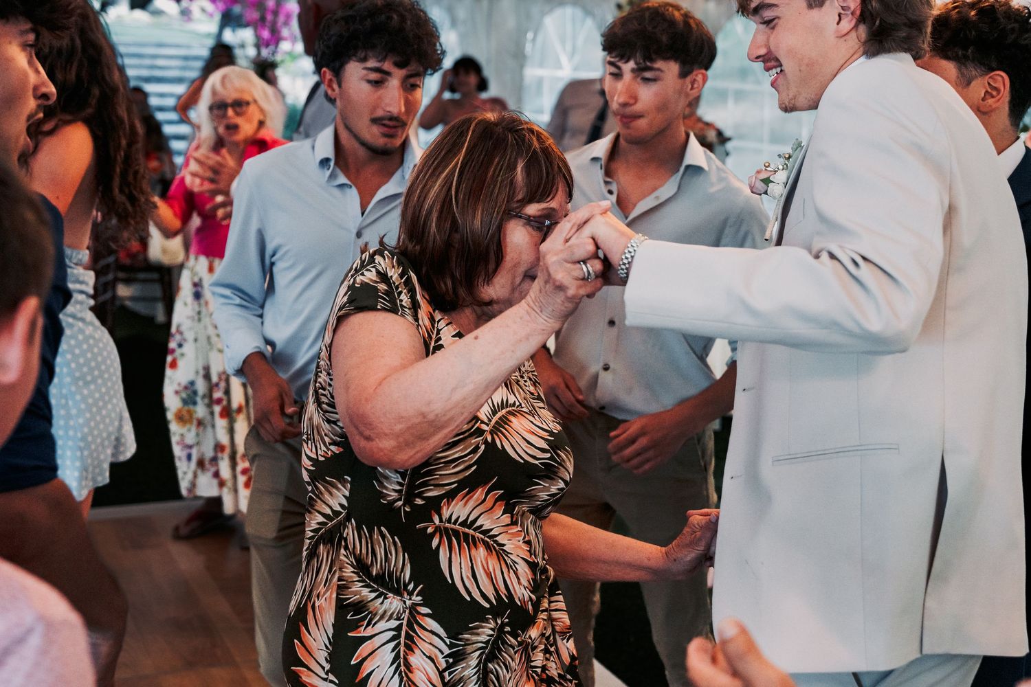 A woman in a floral dress kisses a man's hand while dancing at a festive indoor celebration.
