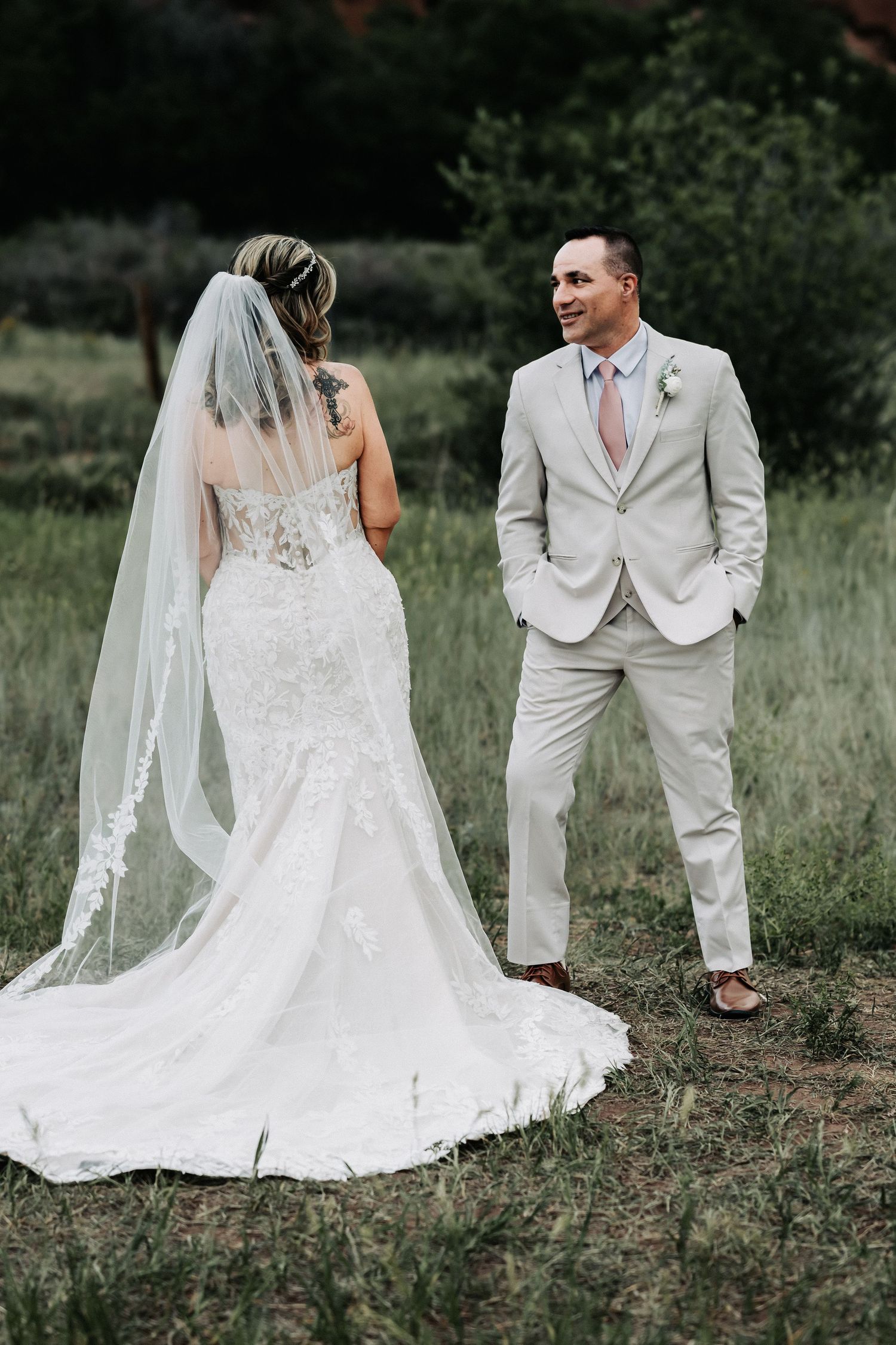 Bride in lace mermaid gown with veil and groom in tan suit share a romantic outdoor moment on their wedding day.