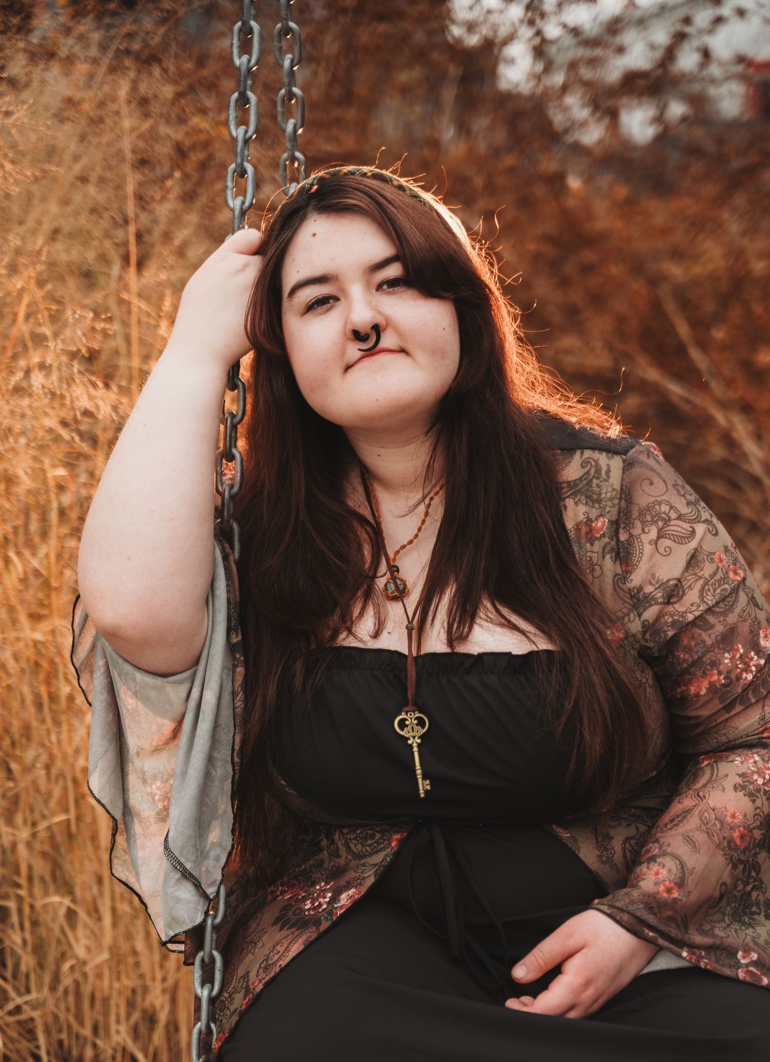 A person in a black top with sheer lace sleeves poses in autumn lighting while holding onto a swing chain.
