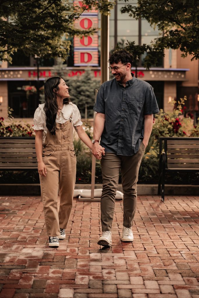 Couple walking hand in hand on brick pathway in casual attire during lifestyle photoshoot.