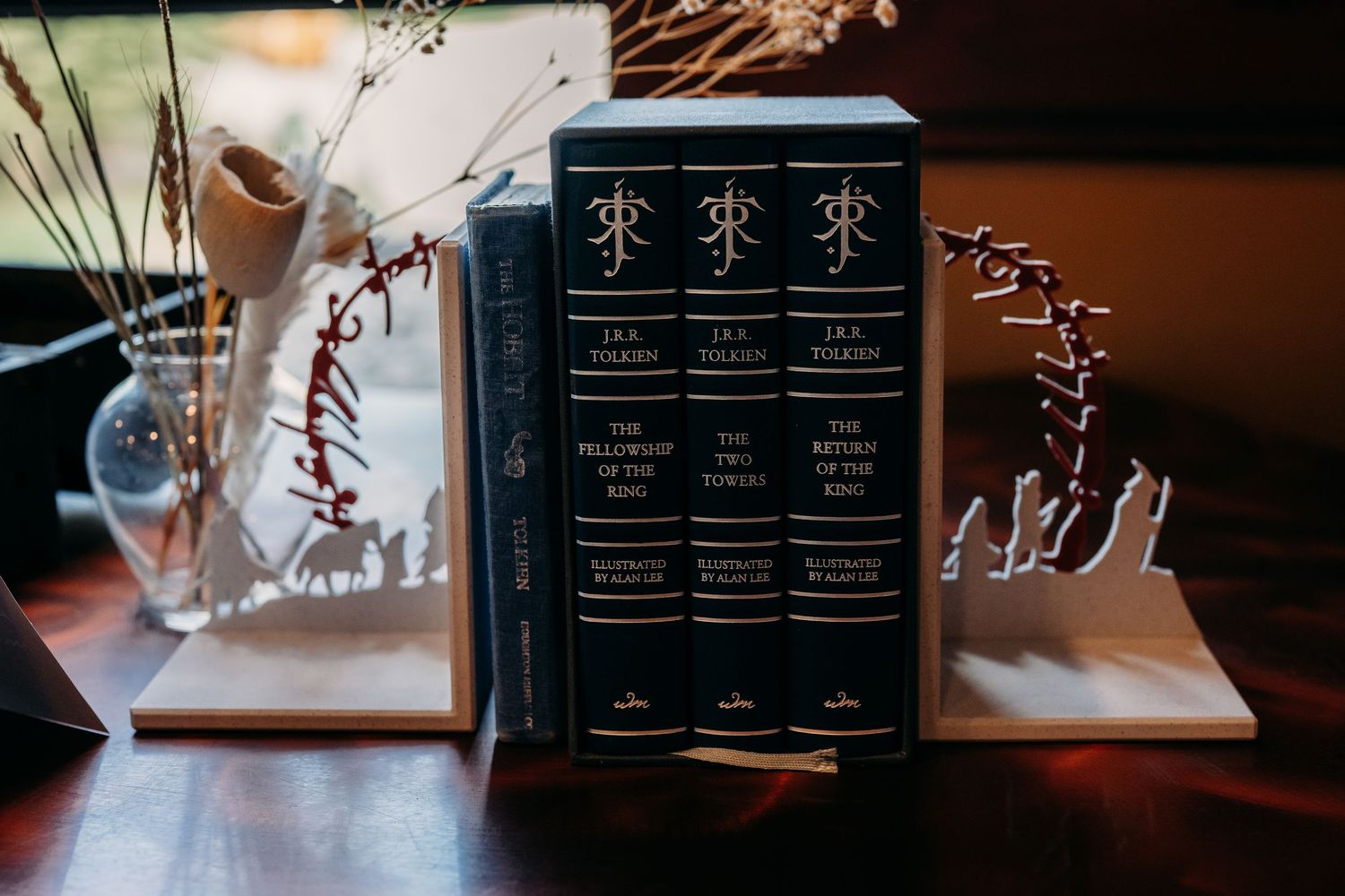 Three J.R.R. Tolkien Lord of the Rings hardcover books displayed between decorative bookends on a wooden table.