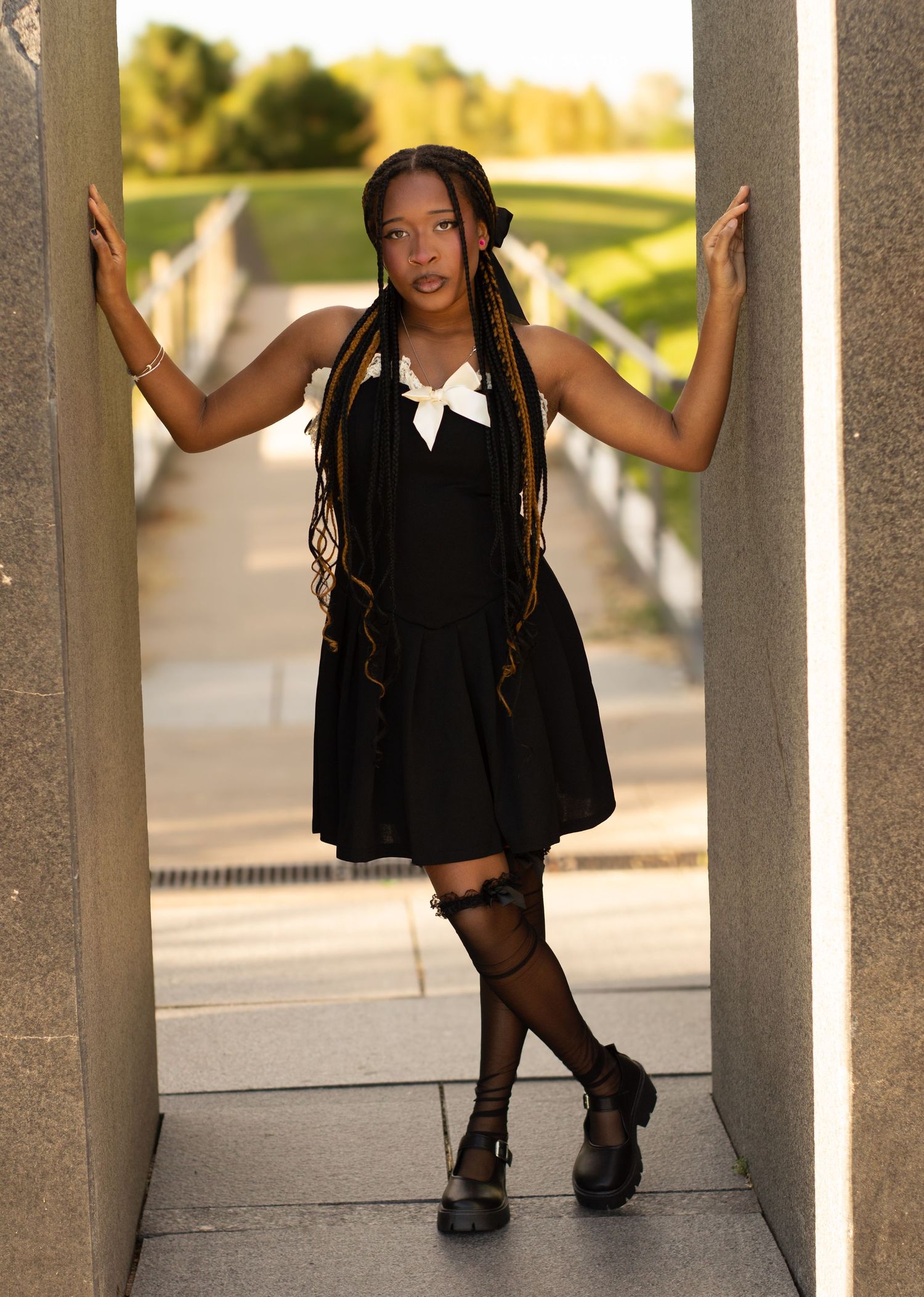 Stylish black dress and knee socks pose between concrete pillars outdoors.