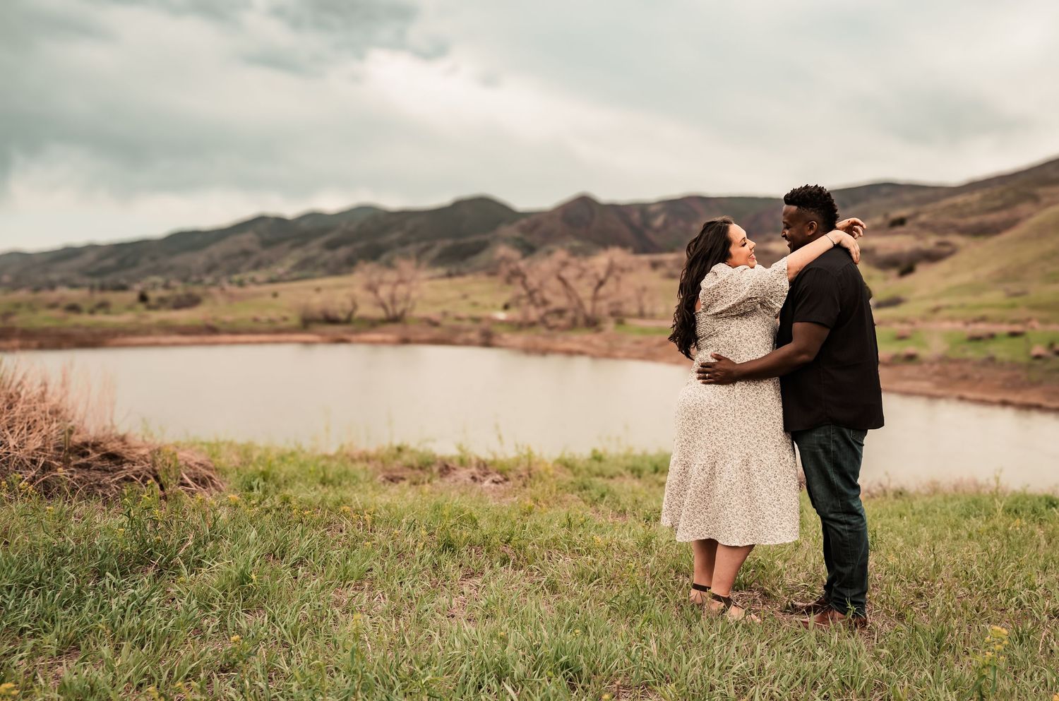 A romantic couple poses for photos in a scenic outdoor mountain landscape.