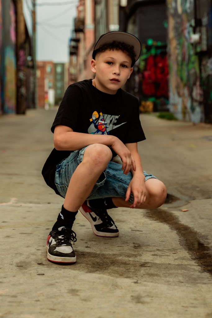 Athletic pose in casual streetwear against urban graffiti background.