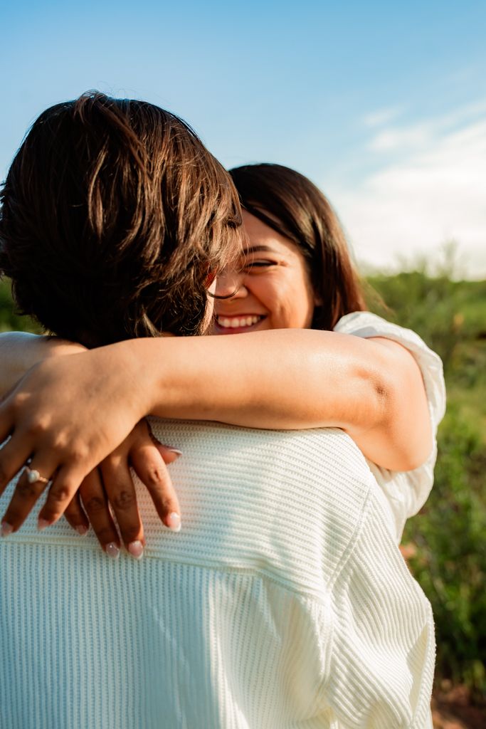 A joyful outdoor embrace captured in warm sunlight with a blue sky background.