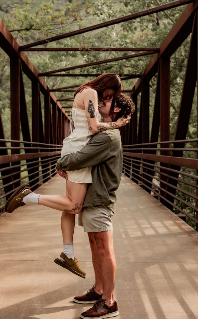 A romantic embrace on a metal bridge surrounded by lush greenery.
