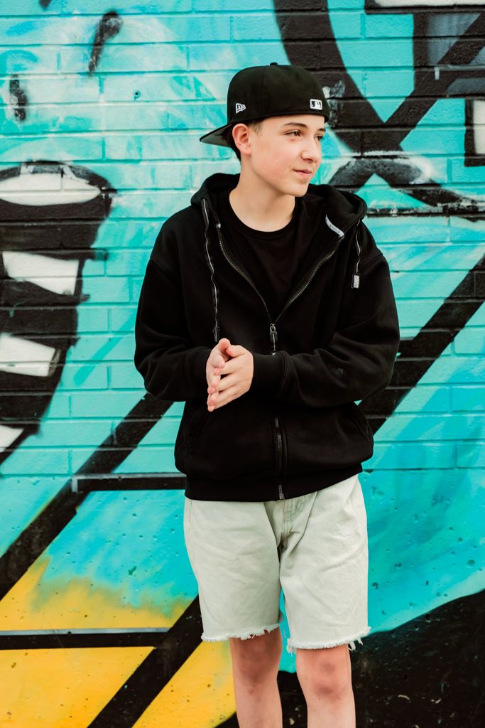 Athletic style photo against turquoise graffiti wall featuring shorts and baseball cap.