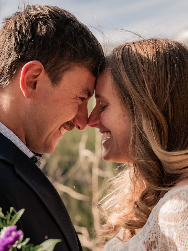 A romantic close-up moment between a couple on their wedding day with foreheads touching and joyful smiles.