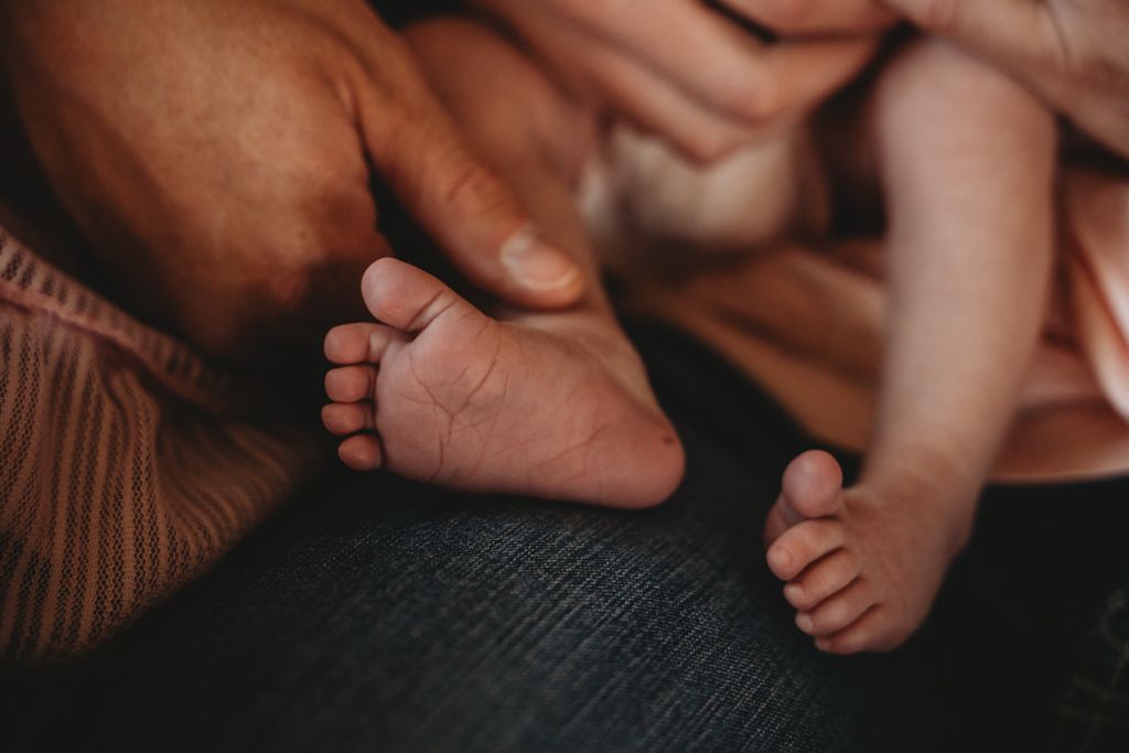 Close-up view of tiny newborn baby feet being gently held by adult hands in warm lighting.