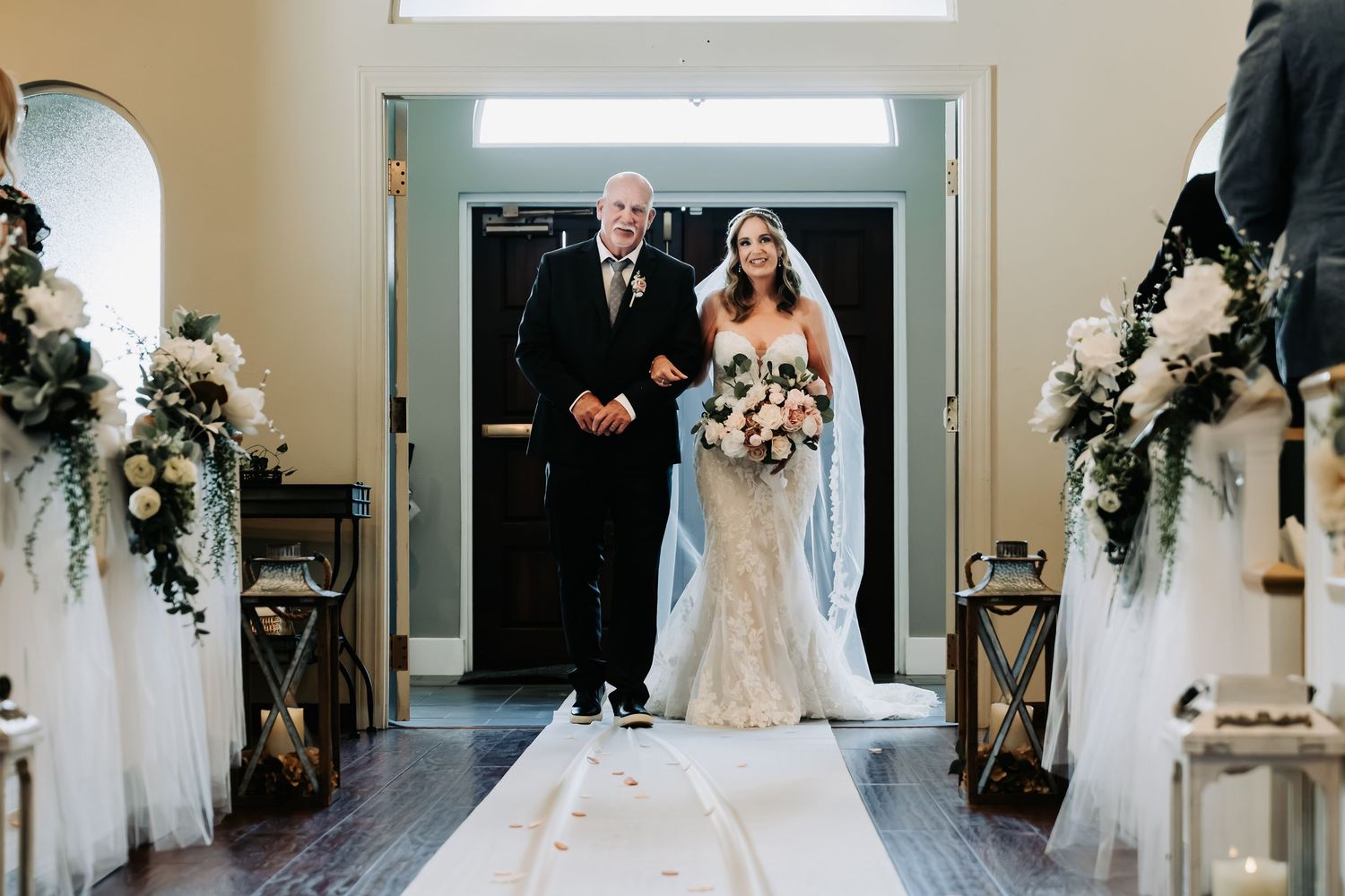 Bride walks down the aisle with her father in a elegant church wedding ceremony with floral arrangements.