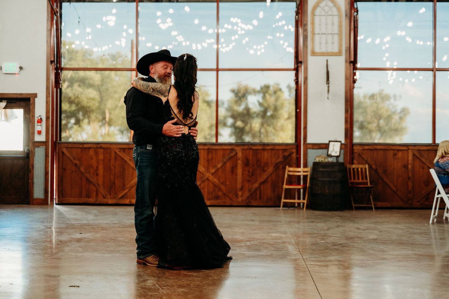 Couple sharing first dance in rustic barn wedding venue with string lights and wooden doors.