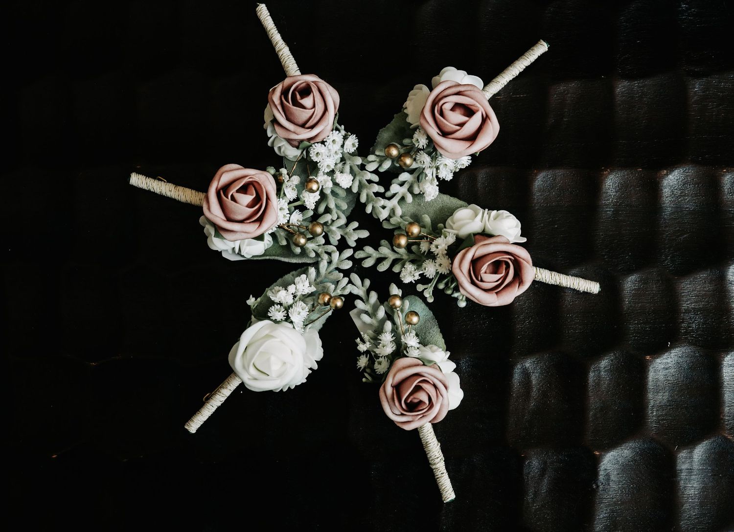 Elegant arrangement of pink and white roses with greenery boutonnieres on dark quilted background.