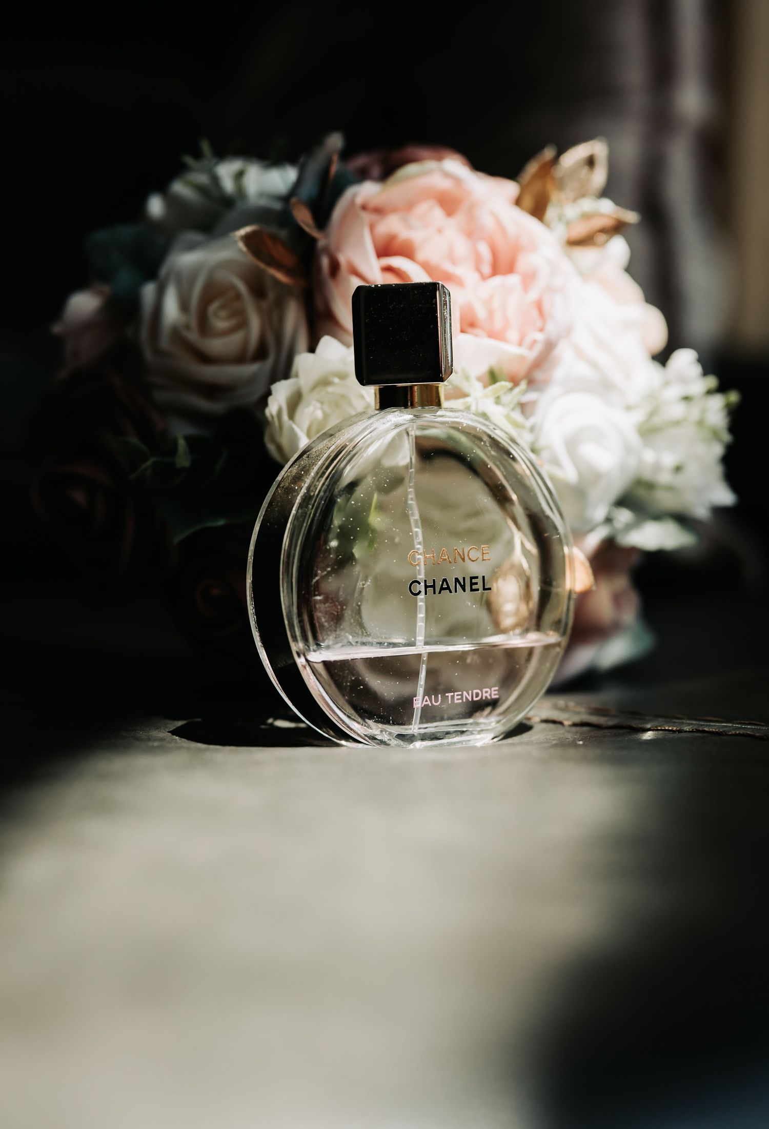 Chanel Chance Eau Tendre perfume bottle with black cap displayed in front of pink and white roses.