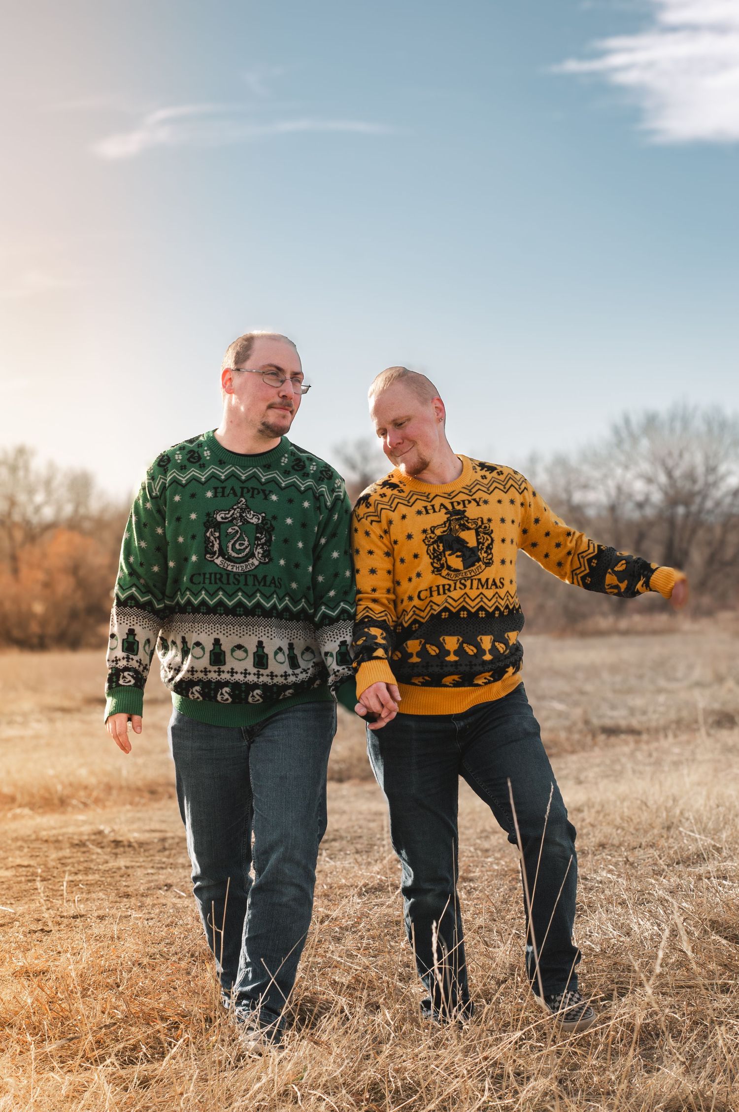 couple in matching Christmas sweaters walking together through a sunlit field.