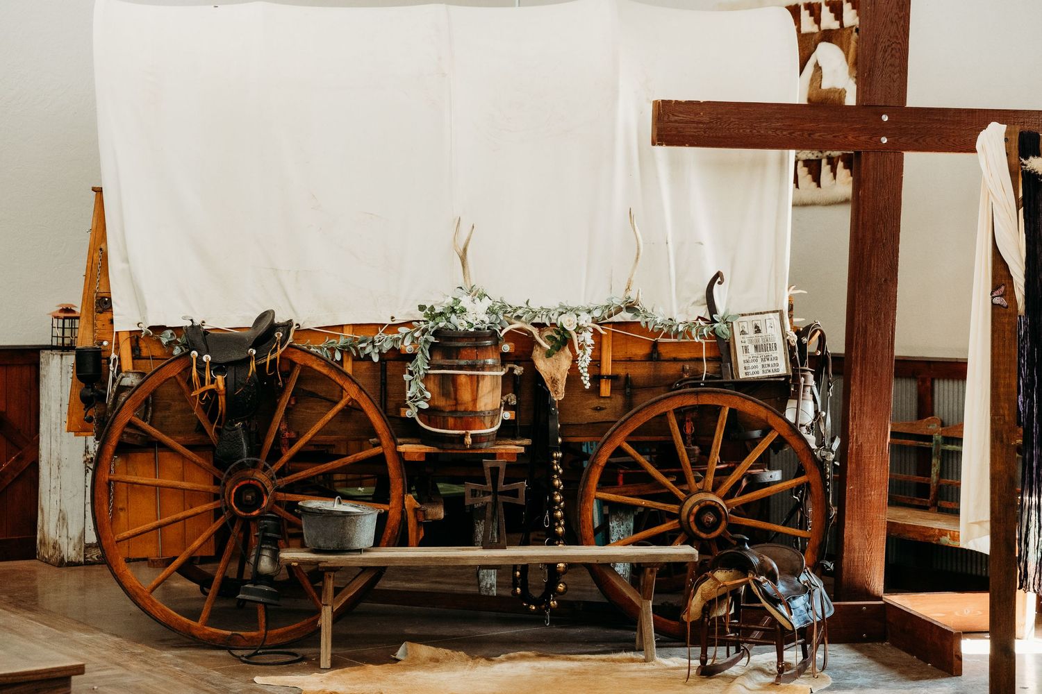 Rustic wooden covered wagon decorated with greenery and pumpkins displayed indoors as a vintage western wedding decor piece.