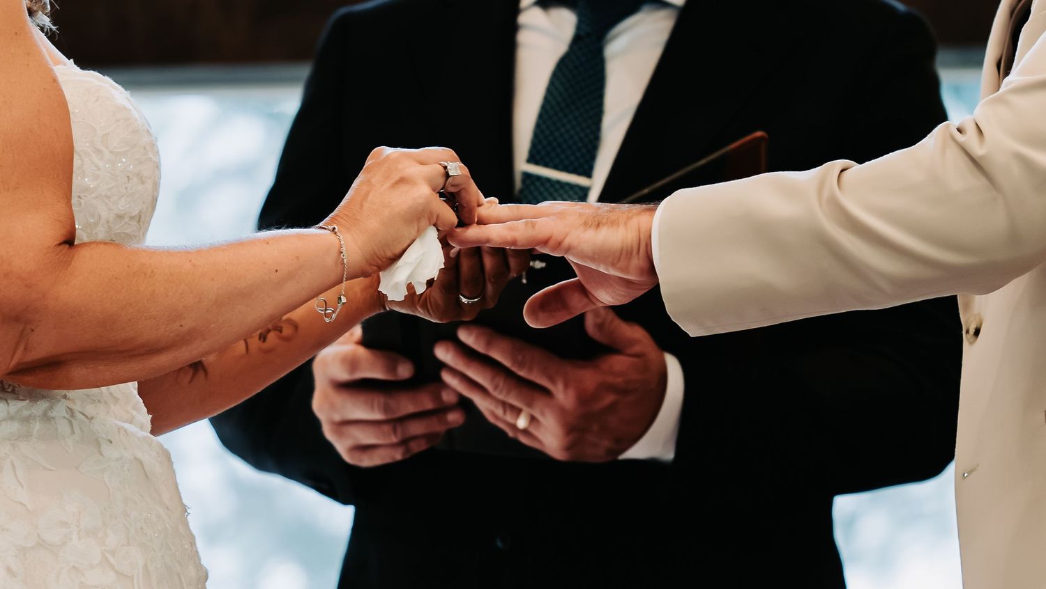 Close-up of bride and groom exchanging wedding rings during ceremony with officiant holding open book.