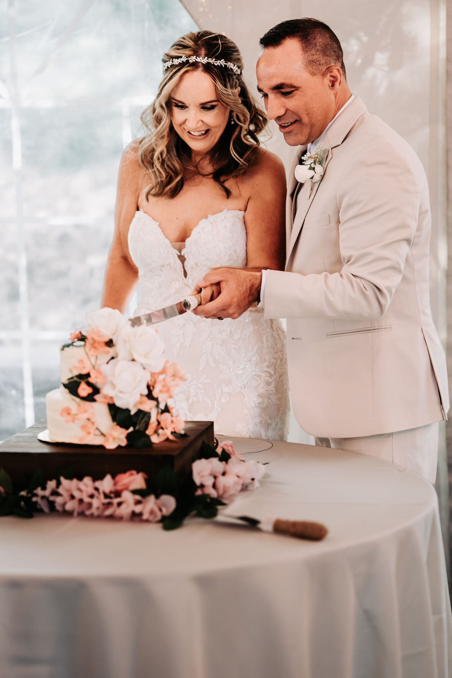 Smiling bride and groom cut their floral wedding cake decorated with peach blooms at reception.