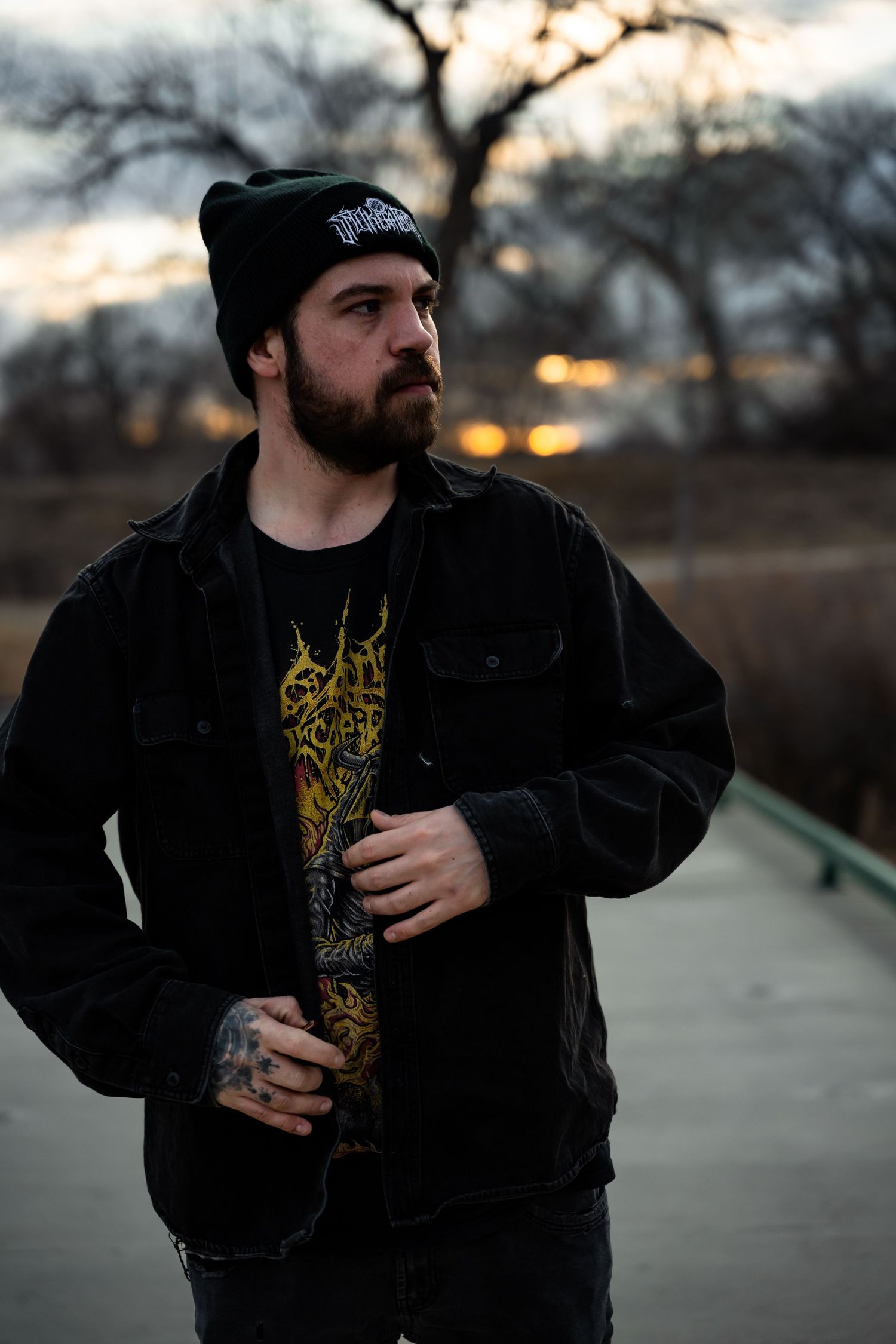 Person in dark hoodie and beanie photographed at dusk on bridge.