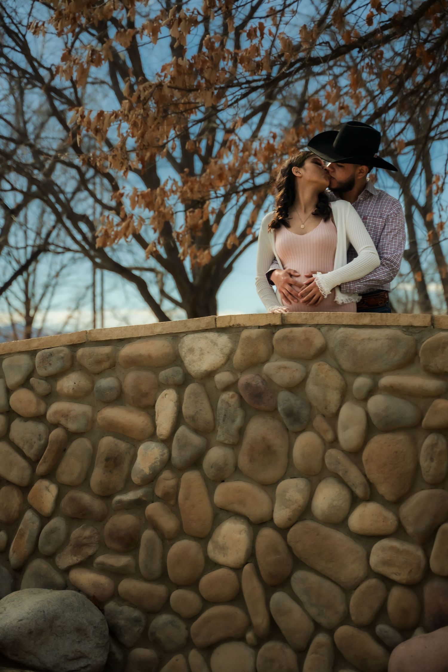 Intimate couple photos against a rustic stone wall with autumn trees in background.