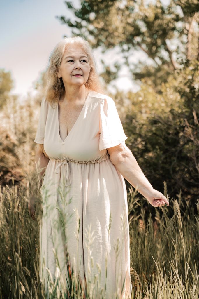 woman wearing a cream-colored dress standing in a field of tall grass on a sunny day.