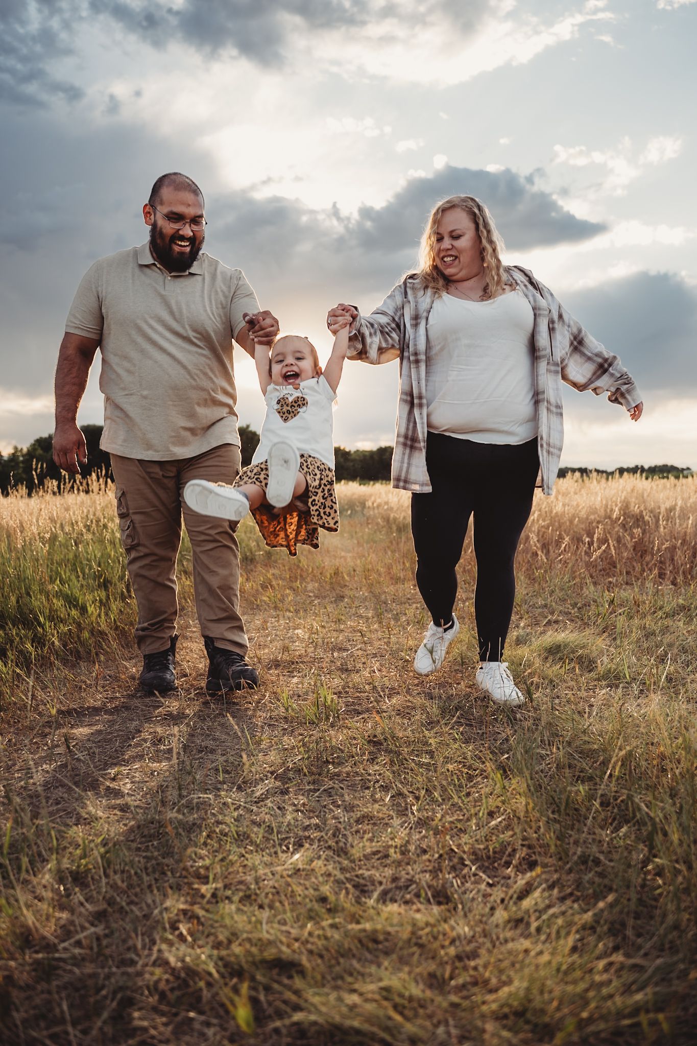 A family walking together through a golden wheat field at sunset while holding hands.