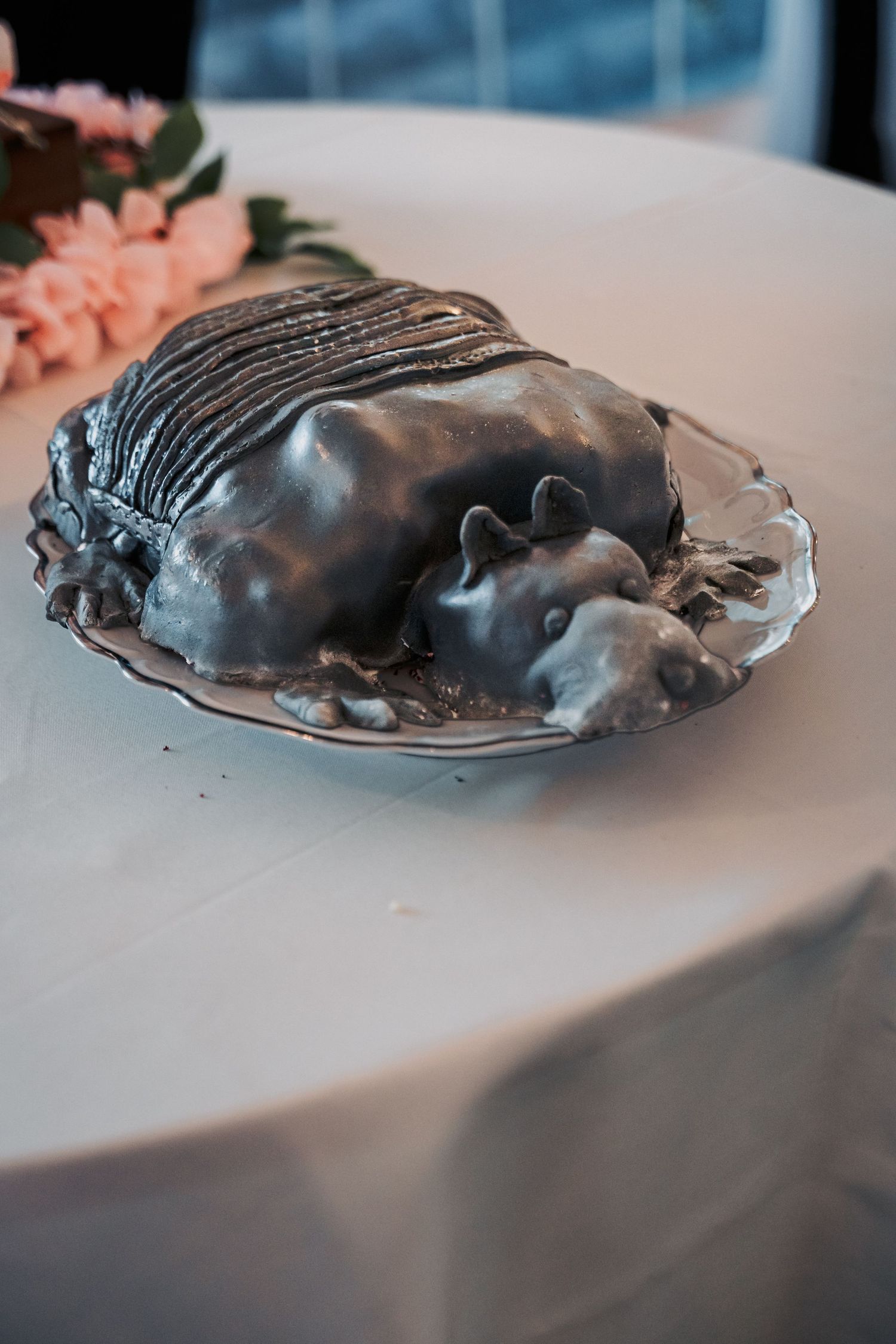 A gray fondant armadillo cake displayed on a plate atop a white tablecloth at an event.