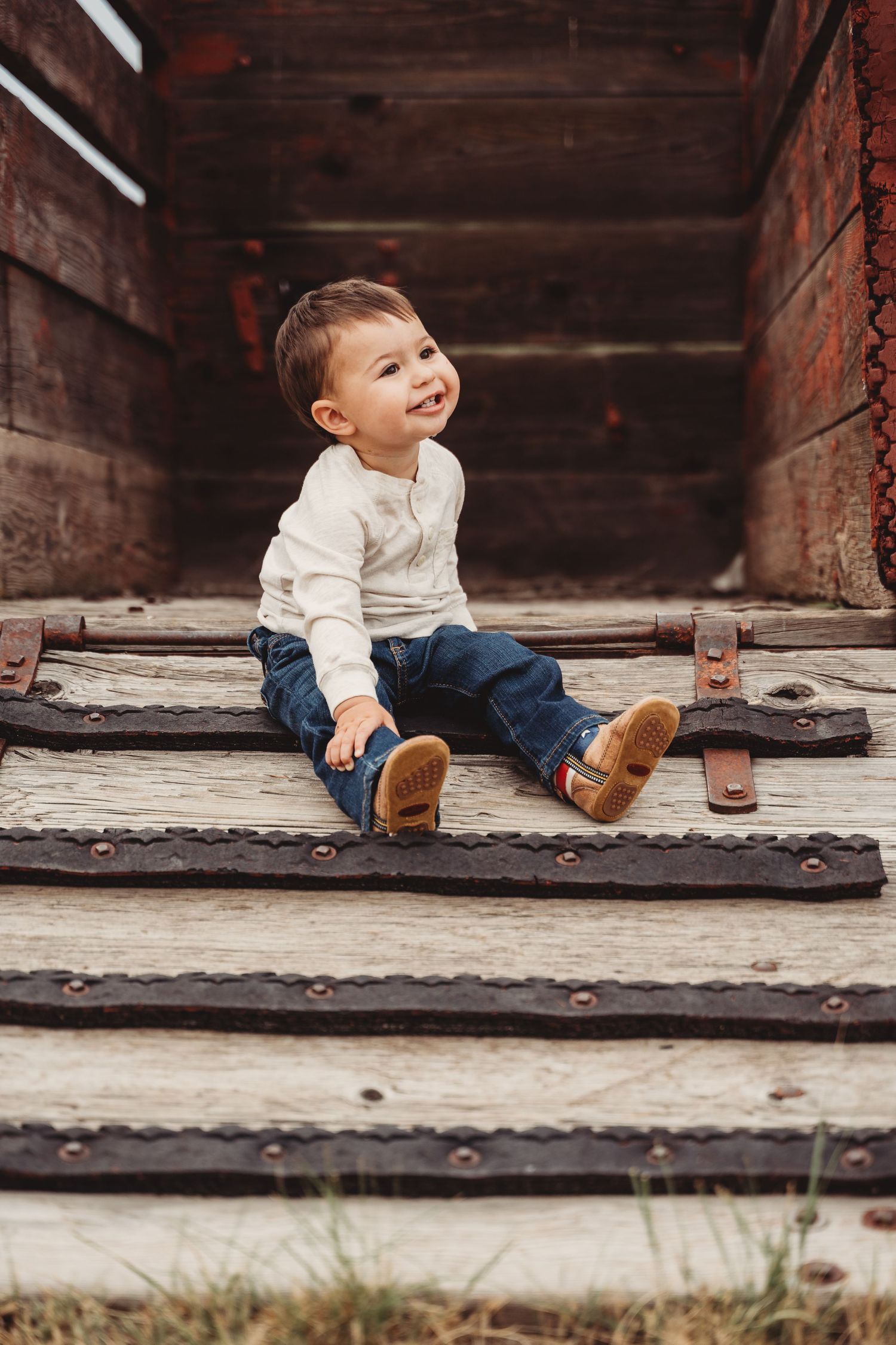 Small child sits on rustic wood porch wearing brown boots and casual clothing in panoramic composite image.
