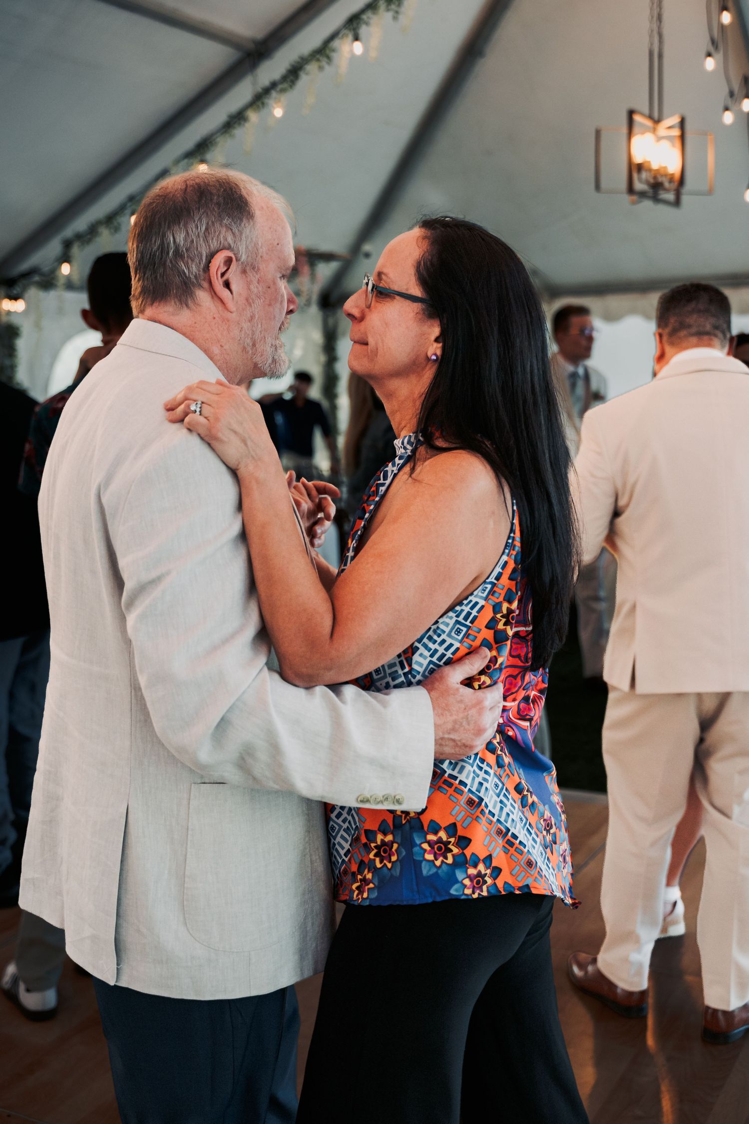 Couple slow dancing together at a wedding reception under a white tent with string lights.