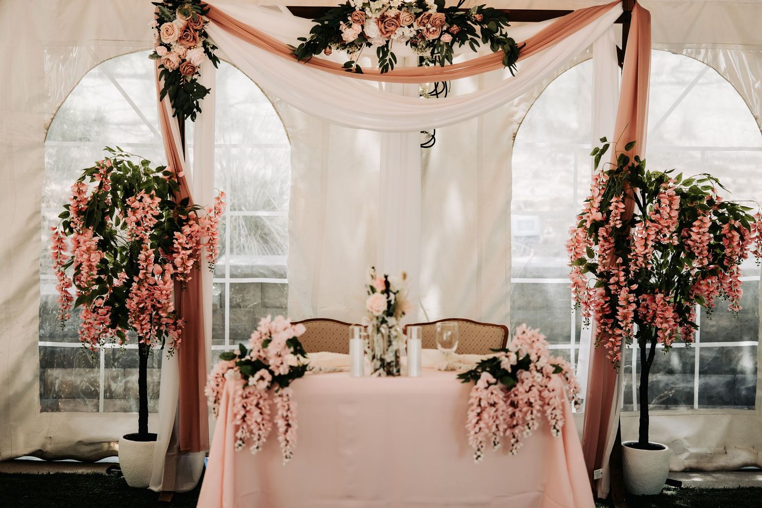 Elegant wedding sweetheart table with pink draping, floral arch, and cascading pink wisteria arrangements.