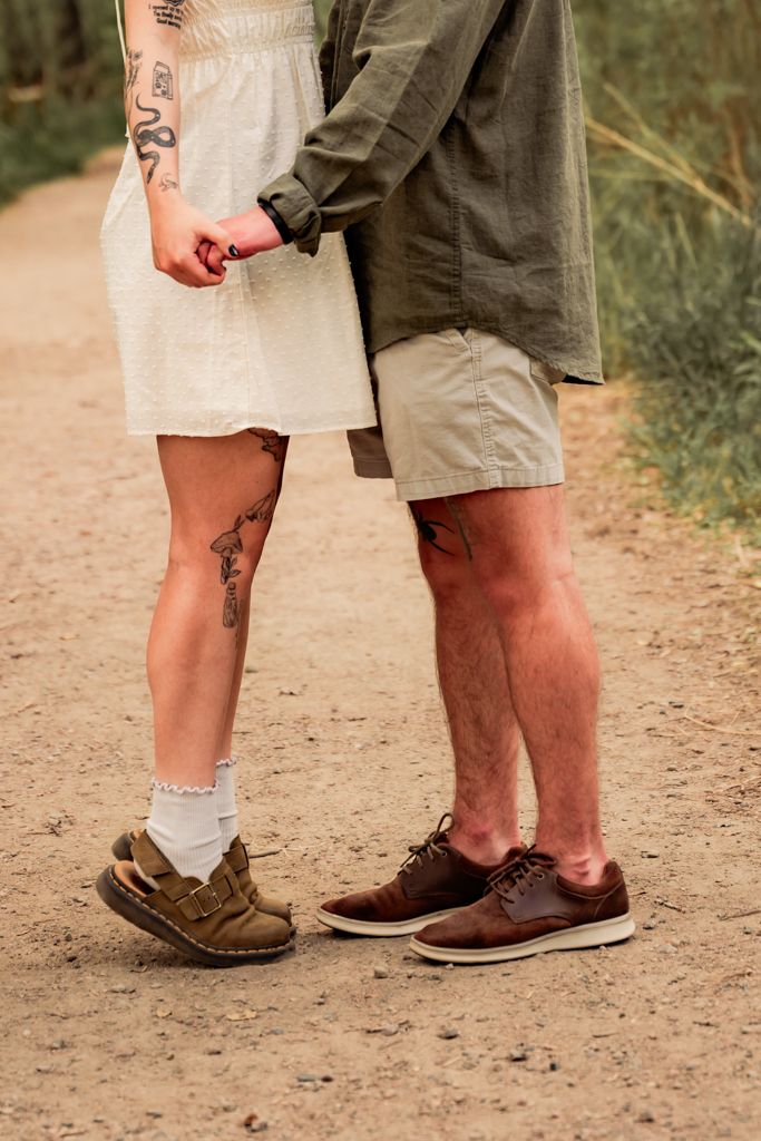Close-up of two pairs of legs wearing brown casual shoes standing together on a dirt path in nature.