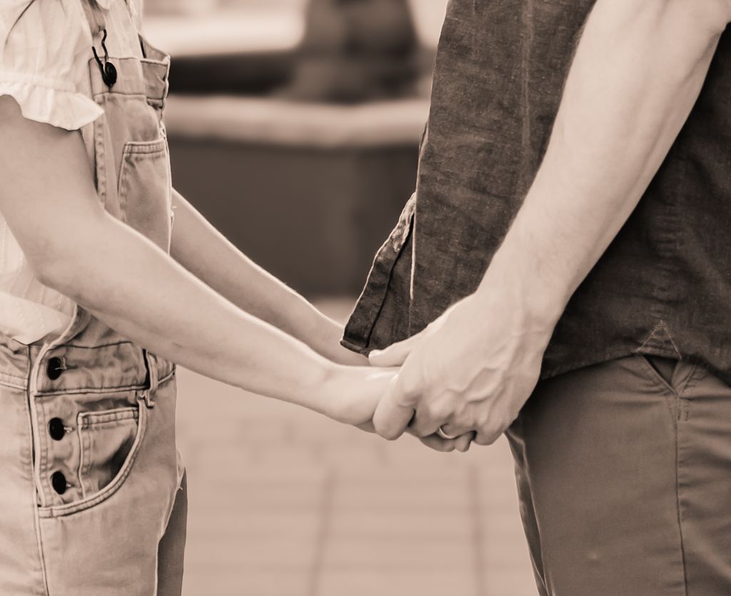Black and white detail shot of couple holding hands while sitting together.