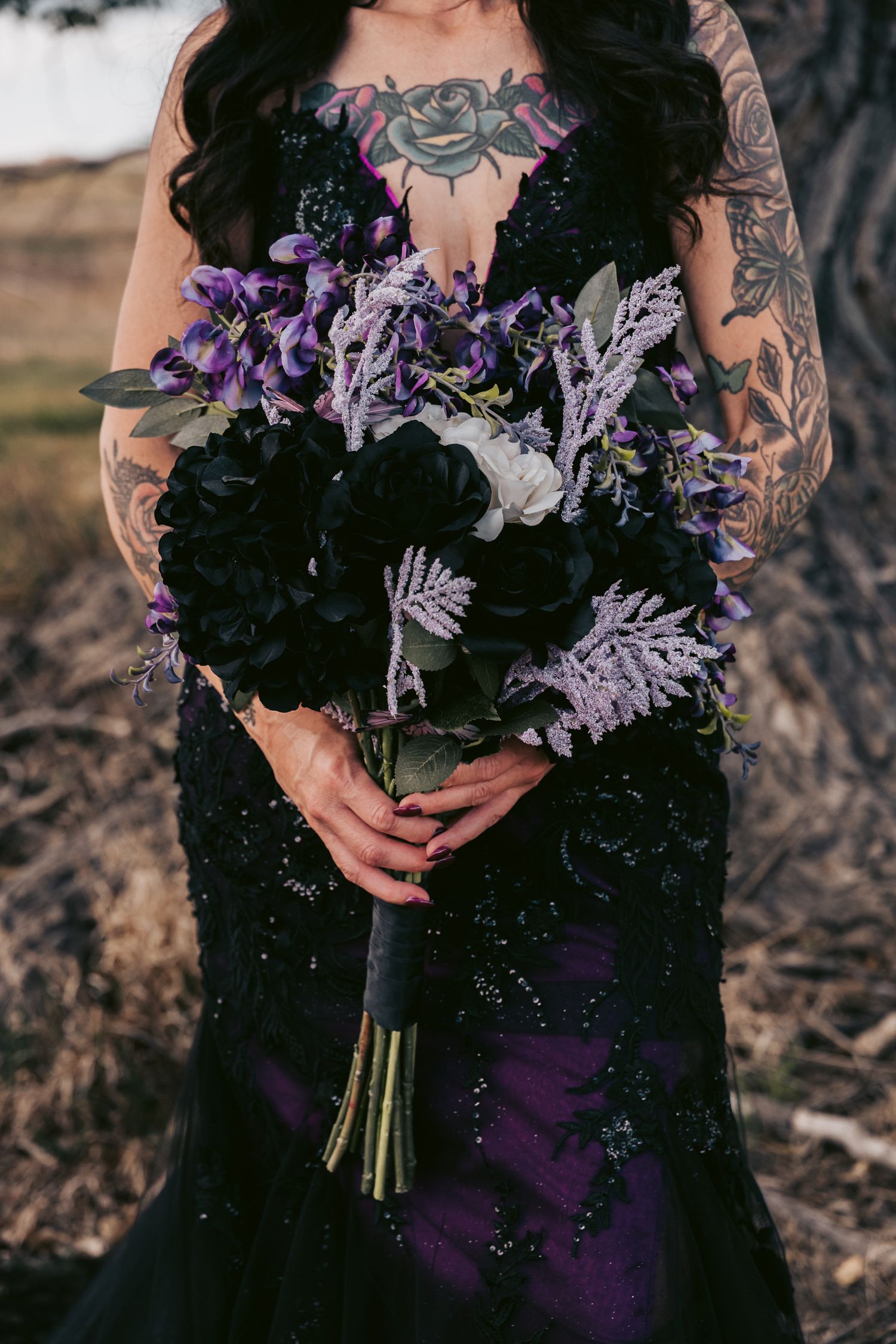 Tattooed bride in black beaded purple gown holding dark floral bouquet with black roses and lavender blooms.