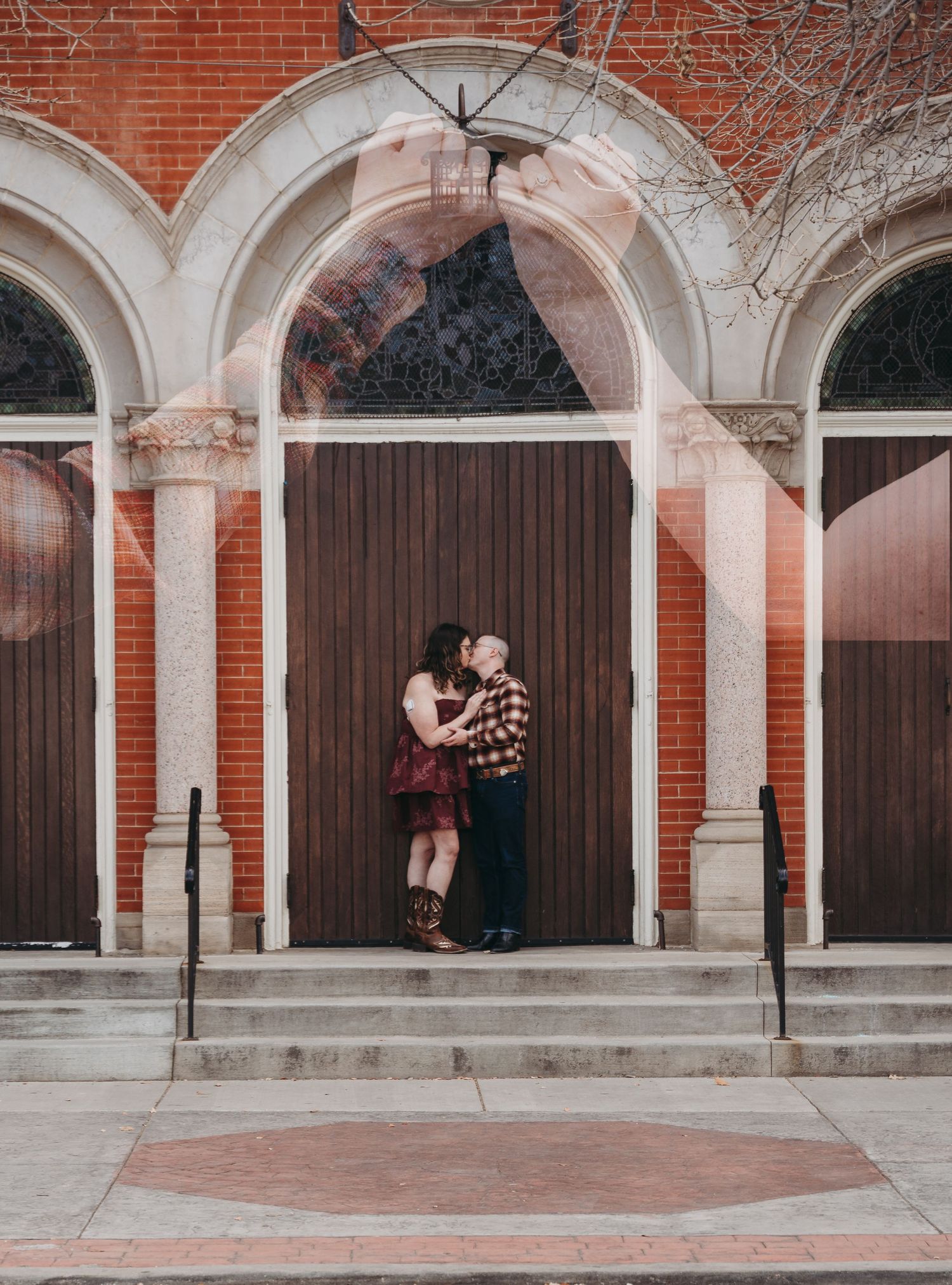 Romantic couple kissing in front of arched wooden doors on brick church steps during engagement photos.