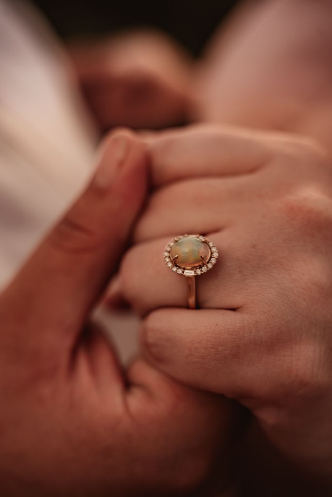Close-up sequence of hands exchanging engagement rings with delicate opal stone in gold setting.