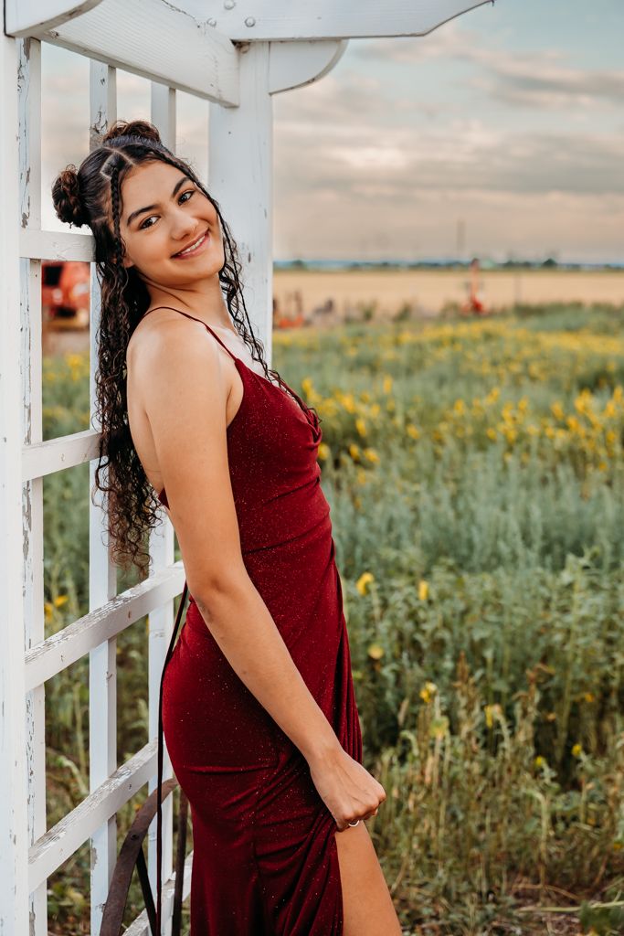 Woman in a burgundy dress poses outdoors in a field of wildflowers during golden hour.