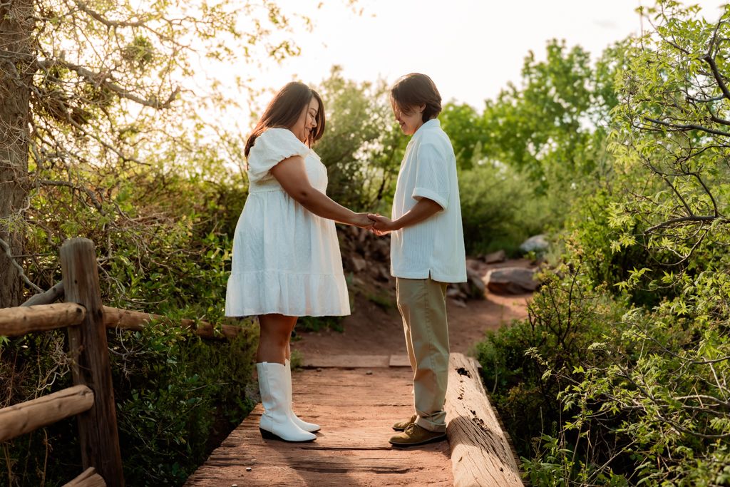 A couple holding hands on a wooden bridge surrounded by lush greenery in summer.