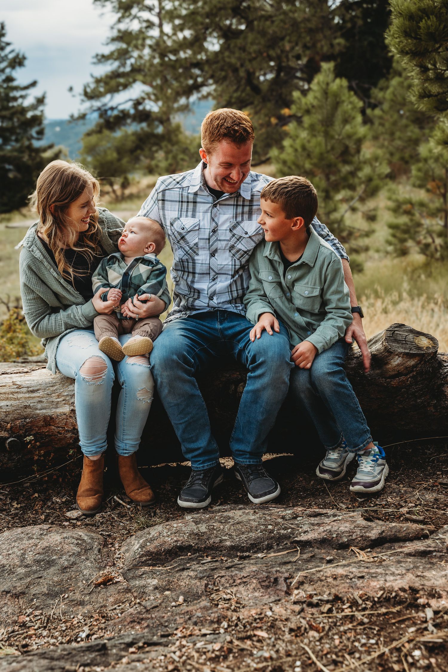 Family sitting together on fallen log in forest setting during outdoor photoshoot.