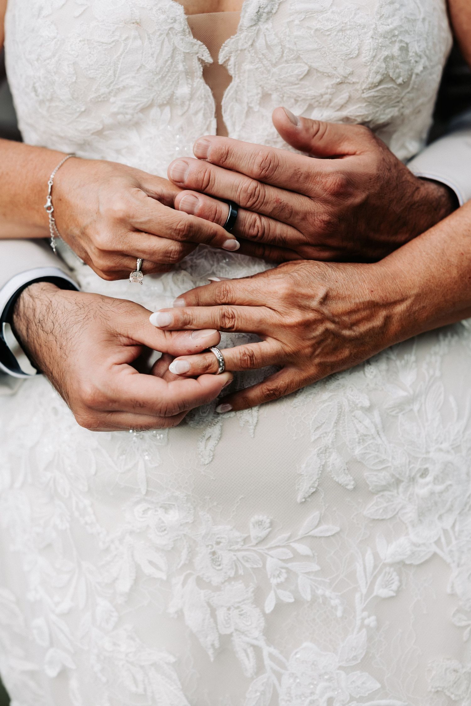 Close-up of bride and groom hands showing wedding rings, bride in white lace dress.